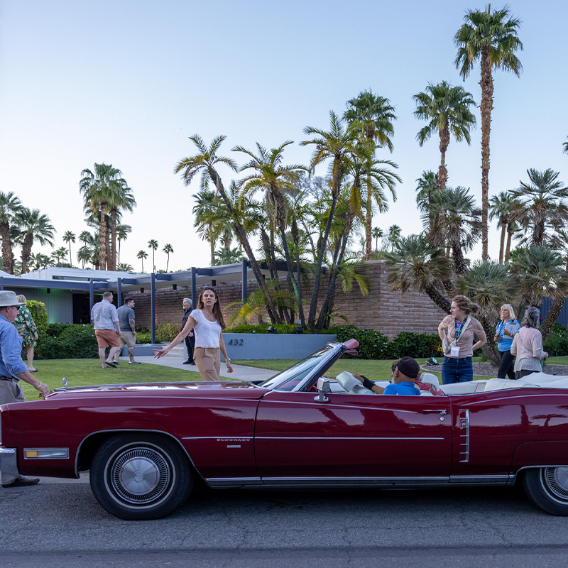 people gather around a red luxury car surrounded by palm trees in Palm Springs