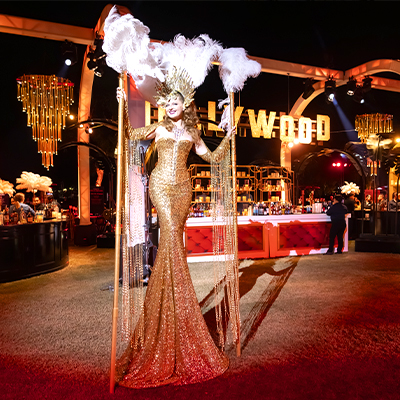 Event performer in gold dress on stilts at a Los Angeles red carpet-style event